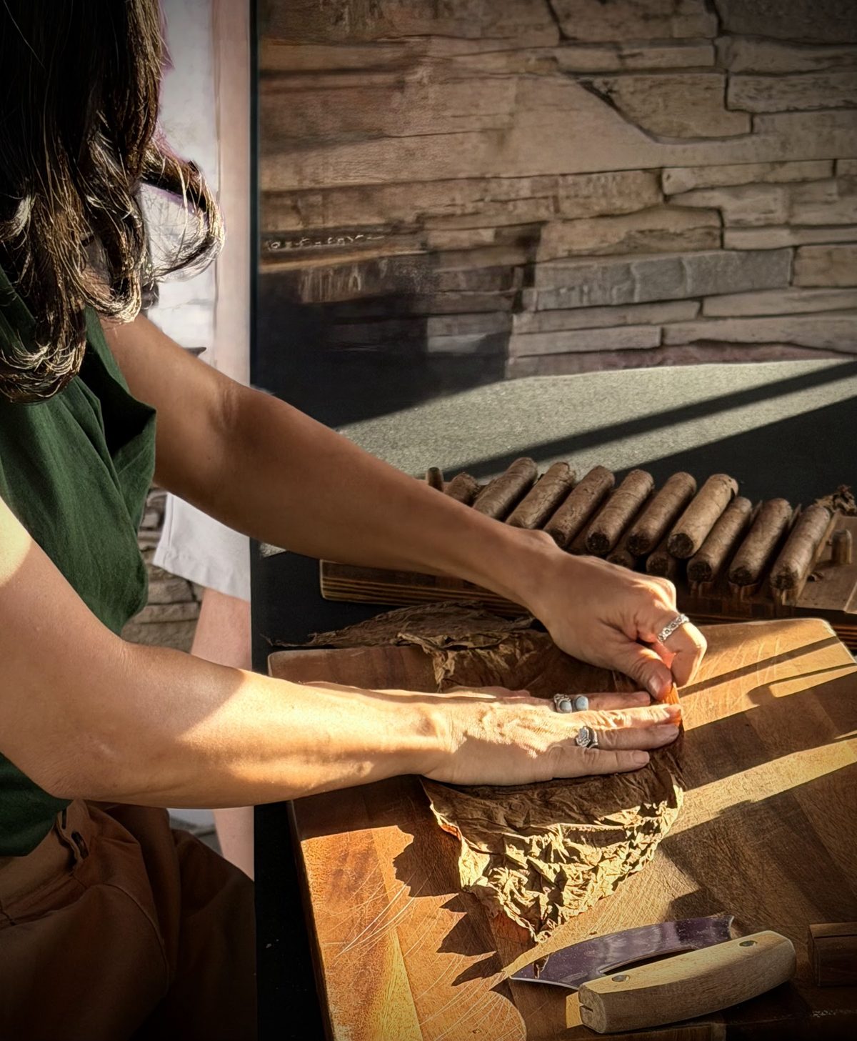 A Don Valdi roller shaping a tobacco leaf by hand, with finished cigars resting in a wooden mould